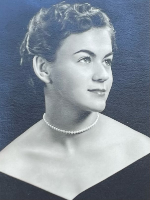 A headshot of Mary Lou wearing a delicate string of pearls